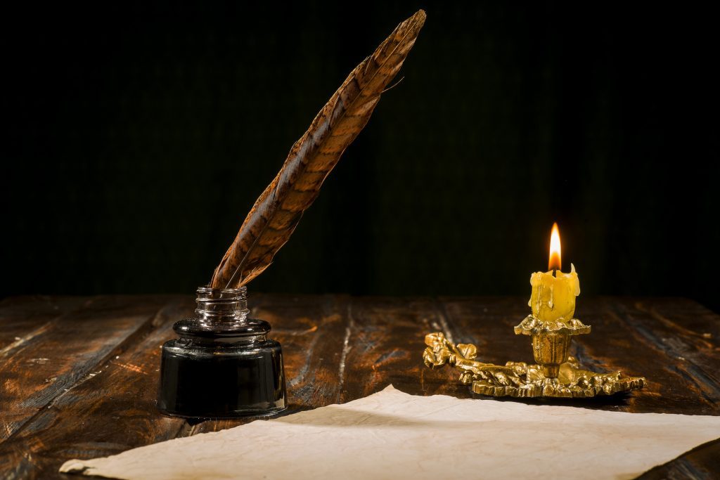 Education and writing concept, pen in ink bottle and candlestick with candle on wooden table on dark background.